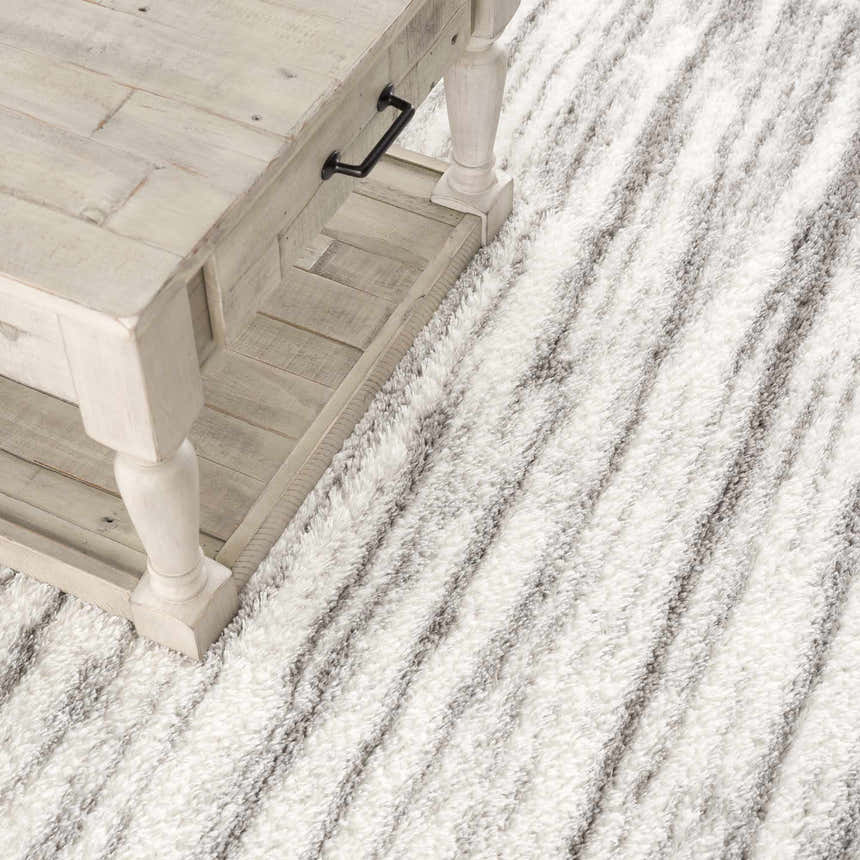 Close-up of the gray and white striped Lotta Area Rug, a shag rug with a soft texture, styled with a whitewashed wood table. Styleshot