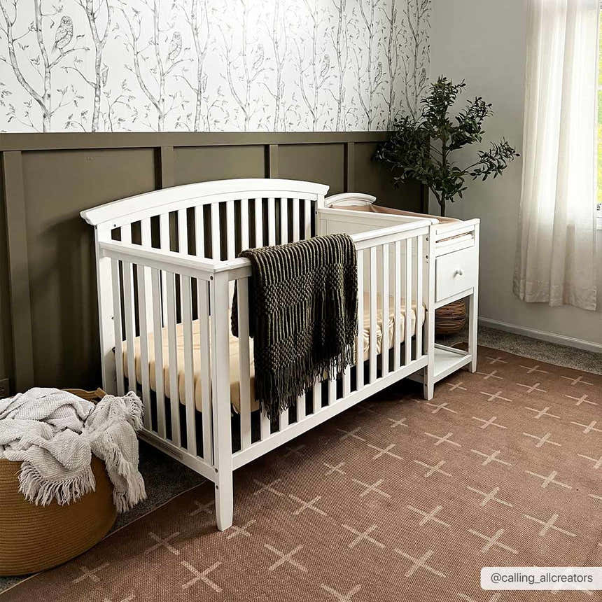 Nursery scene with a white crib and the Haimi Washable Area Rug in brown with a plus sign pattern on the floor. Roomscene-Rectangle