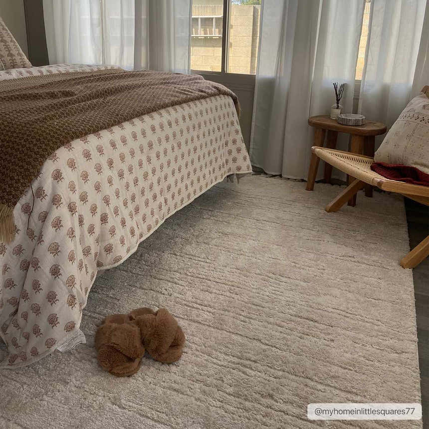 Bedroom scene with Ibarra Textured Ivory Rug, bed with patterned bedding, wooden chair, and slippers on the rug. Roomscene-Rectangle
