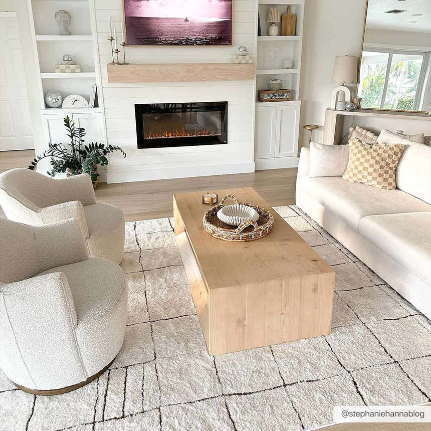 Living room scene with a beige Keanu Area Rug, white sofa and chairs, and light wood coffee table. Roomscene-Rectangle
