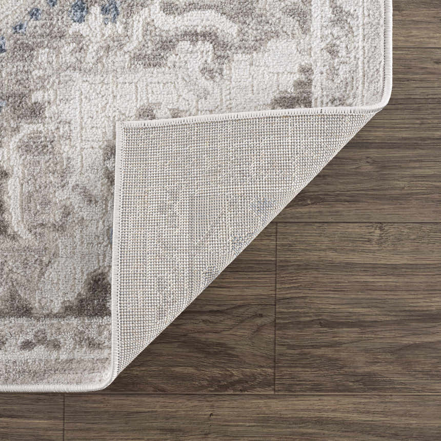 Close-up of the Bakir Area Rug showing its blue and gray traditional pattern and machine woven construction on wood floors. Fold