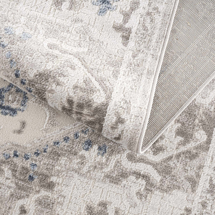 Close-up of the Bakir Area Rug. Machine woven rug in blue and gray with a traditional pattern and textured pile. Fold