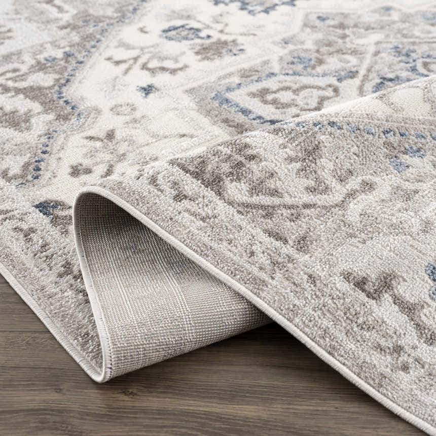 Close-up of the Bakir Area Rug, a machine-woven rug in blue and gray with a traditional design and visible rug backing. Fold