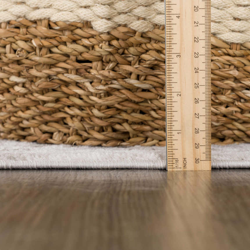 Close-up of the Bakir Area Rug showing pile height with a ruler. Gray rug next to a woven basket on a wood floor. Pile