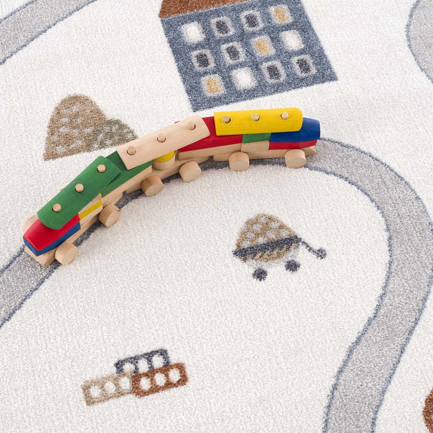 Close-up of the Olwen Washable Area Rug with a road and building pattern in blue, cream, and gray. Wooden toy train on rug. Styleshot