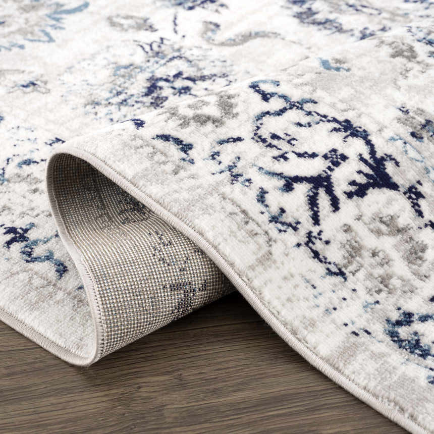 Close-up of the Duena Area Rug showing its blue and light gray traditional vintage pattern and machine-woven construction. Fold