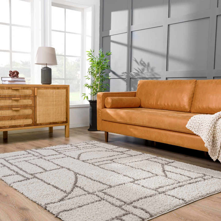 Living room scene with a geometric Andia Gray Area Rug, tan leather sofa, and wood cabinet. Roomscene-Rectangle