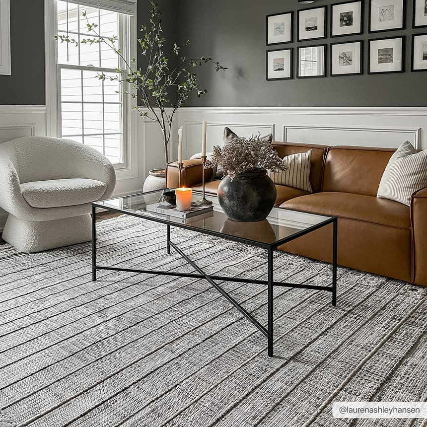 Living room scene with a Naivasha Elegant High/Low Area Rug in charcoal and cream, leather sofa, and glass coffee table. Roomscene-Rectangle