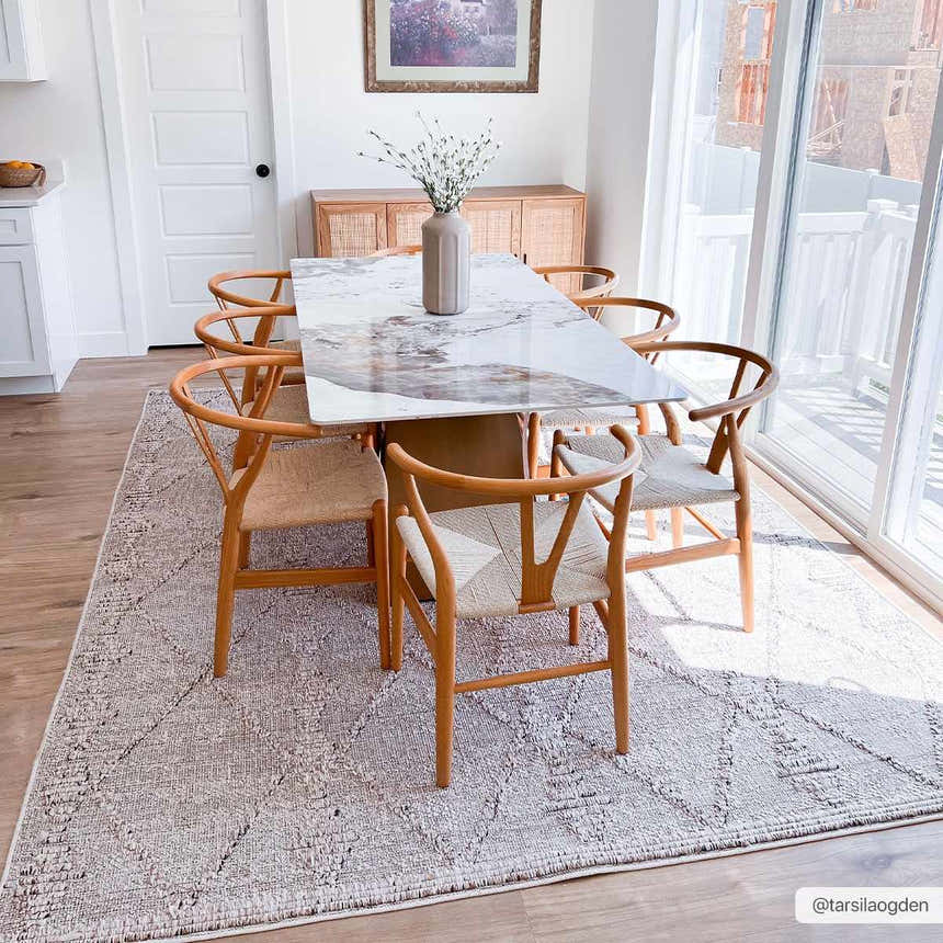Dining room with Nyla Bone rug under a marble table and wooden chairs, bathed in natural light. Roomscene-Rectangle