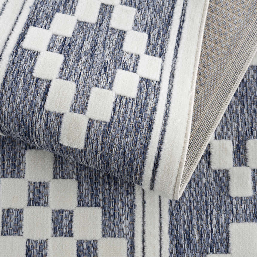Close-up of the Hiro Blue Outdoor Rug showing the denim and white geometric pattern and woven texture. Fold