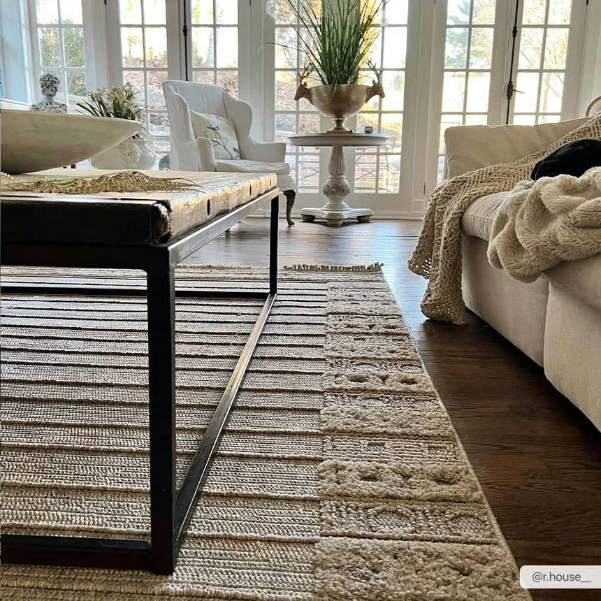 Bright living room with a Sulak Cream Area Rug, dark wood floors, and a rustic coffee table. Roomscene-Rectangle