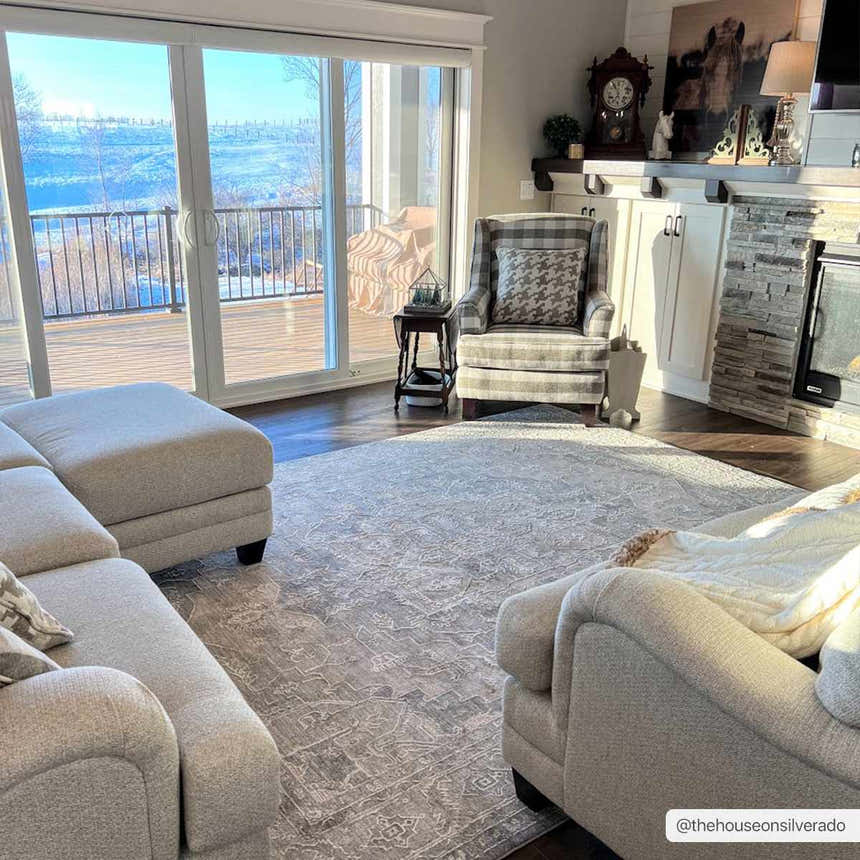 Living room scene with a gray Ulubey Distressed rug, sectional sofa, fireplace, and large windows overlooking a snowy landscape. Roomscene-Rectangle