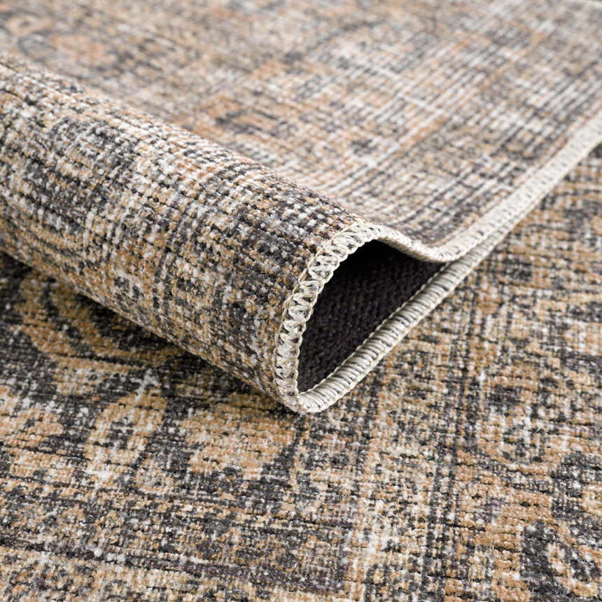 Close-up of the Orsin Washable Area Rug showing its traditional pattern, brown, gray, and white colors, and soft, textured weave. Fold