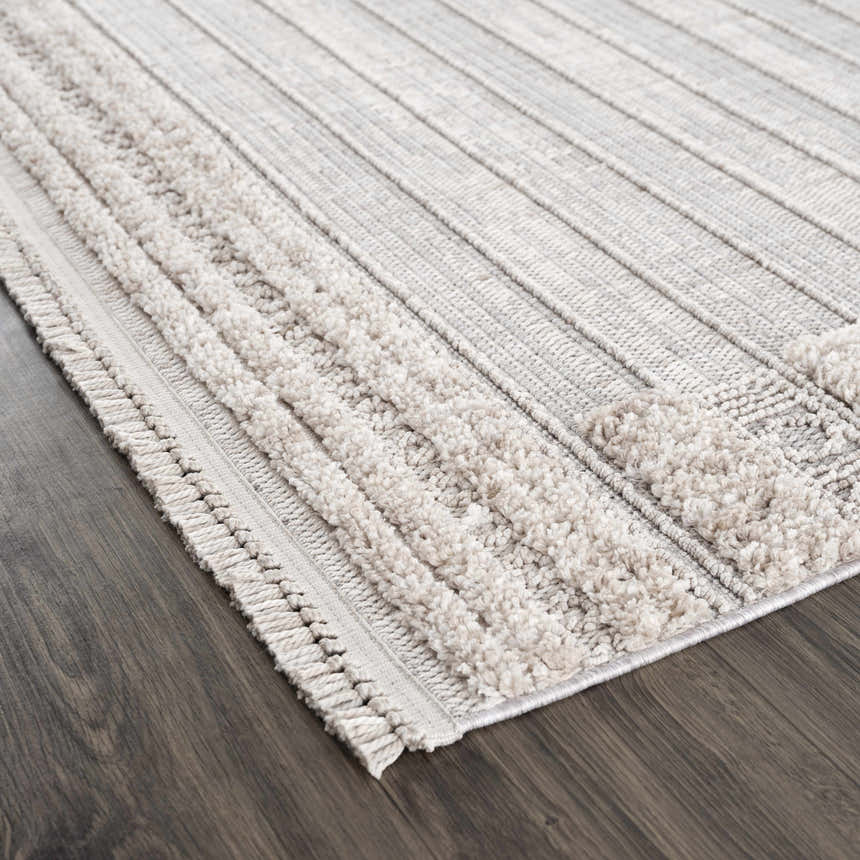 Close-up of Sulak Cream Area Rug showing textured stripes and fringe detail on a dark wood floor. Corner