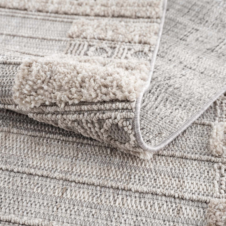 Close-up of Sulak Cream Area Rug showing the textured weave, cream shag accents, and light gray tones. Fold