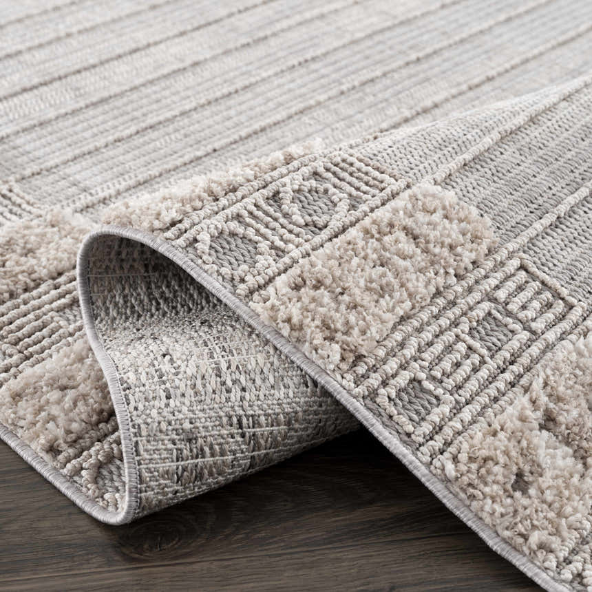 Close-up of the Sulak Cream Area Rug showing its charcoal, cream, and beige geometric pattern and textured pile. Fold