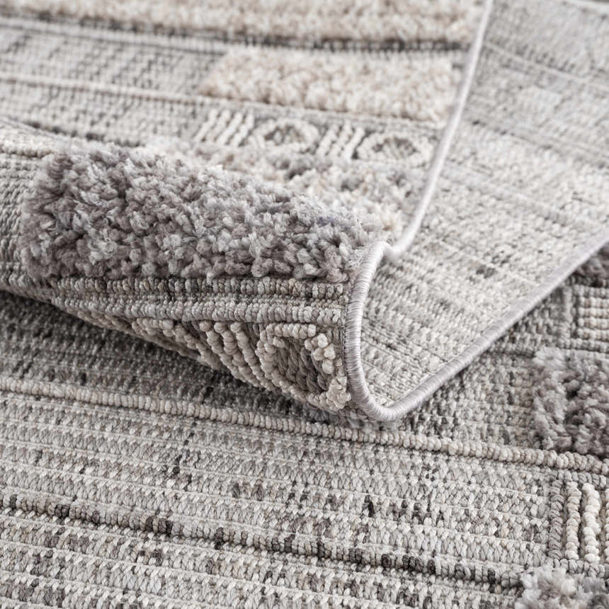 Close-up of the Naivasha Elegant High/Low Area Rug, showing its charcoal, cream, and gray textured pattern. Fold
