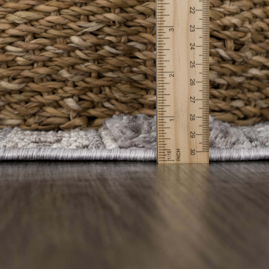 Close-up of the Naivasha rug pile height in light gray, cream, and charcoal with a ruler and basket. Pile
