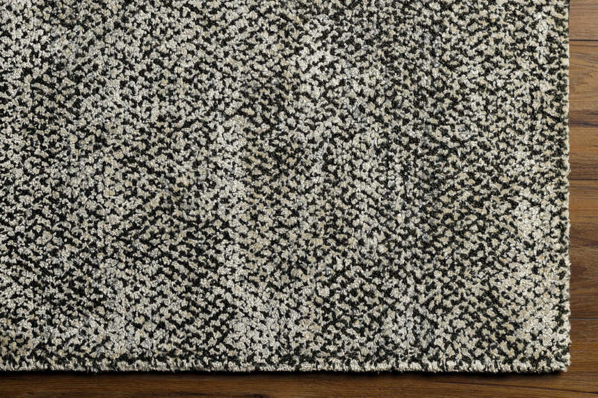 Close-up of the Abiba Area Rug showing its beige and black contemporary design and hand-loomed texture on a wood floor. Corner