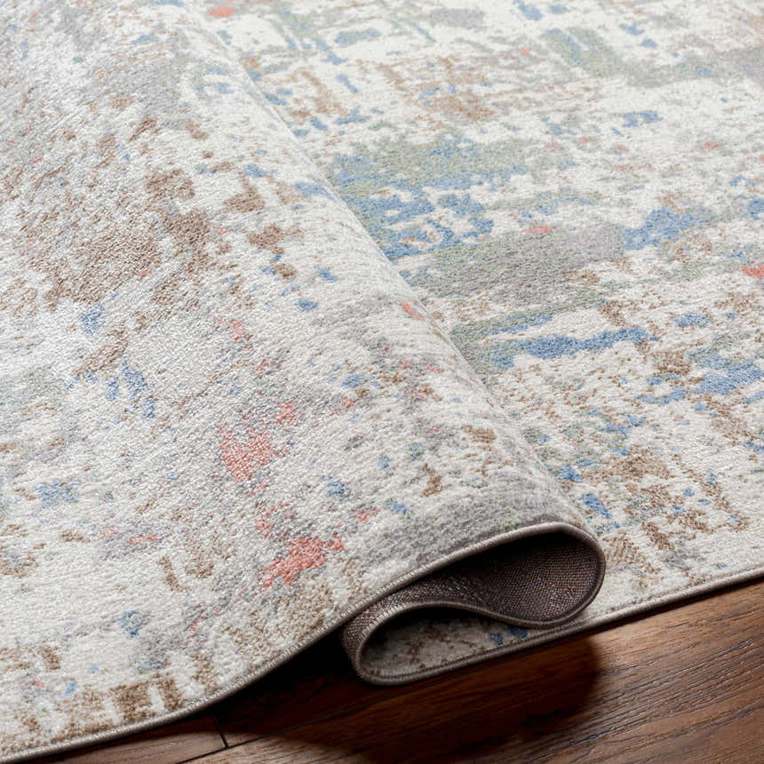 Close-up of the Ahava Washable Area Rug. Features an abstract pattern with blue, brown, and gray hues. Machine woven texture. Fold