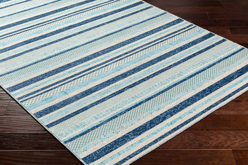 Close-up of the Alain Area Rug, a coastal style rug with blue and white stripes on a dark wood floor. Corner