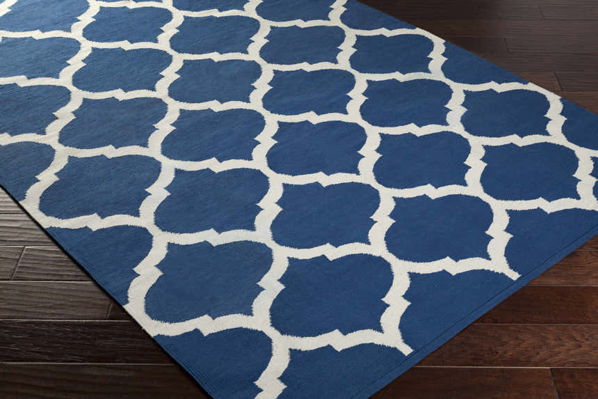 Close-up of the Alcalde Area Carpet on dark wood floors. Features a bright blue and ivory quatrefoil pattern. Hand woven cotton rug. Corner