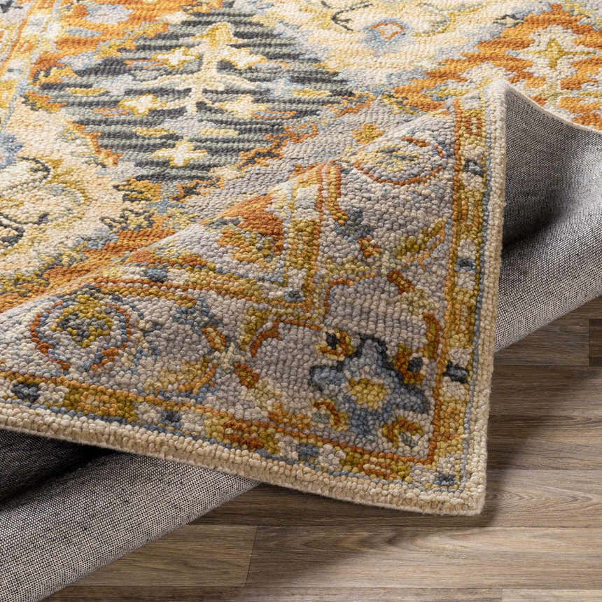 Close-up of the hand-tufted Alliance Area Rug. Features an ornate, traditional pattern in shades of orange, blue, and gray. Fold