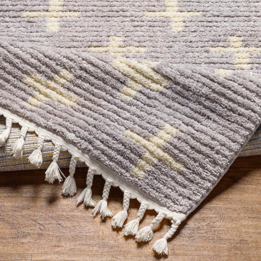 Close-up of the textured Anda Area Rug. Ivory and medium gray stripes with braided tassels. Fold