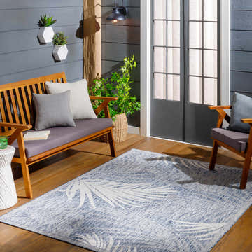 Coastal porch scene with wood furniture and blue Andy Area Rug featuring a palm leaf design. Roomscene-Rectangle