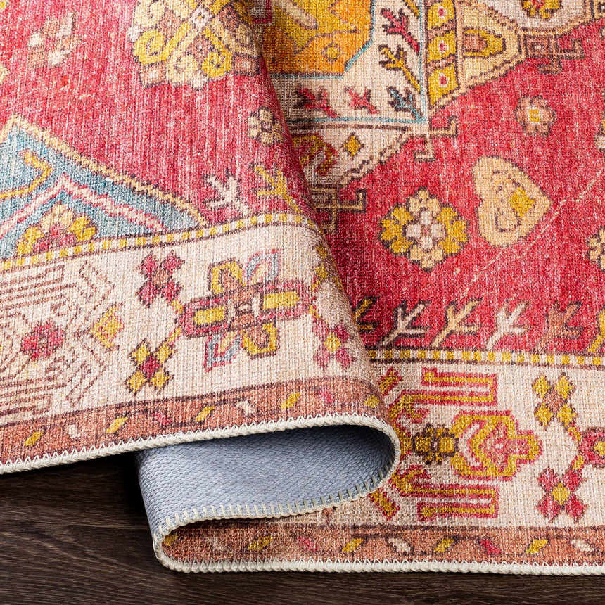 Close-up of the Anopog Washable Area Rug. Features a traditional red, yellow, and blue pattern with a farmhouse style. Fold