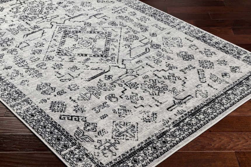 Close-up of the Badar Area Rug featuring a traditional charcoal and gray pattern on a dark wood floor. Corner