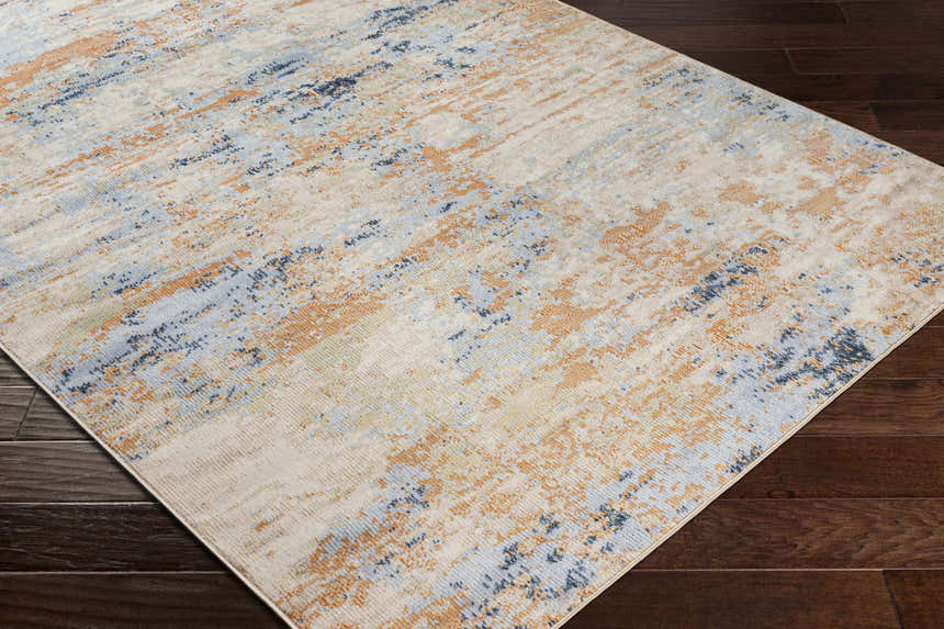 Close-up of the Bagulin Area Rug on dark wood floor. Contemporary design with blue, gold, and cream abstract pattern. Corner