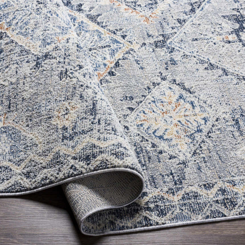 Close-up of Balamban Area Rug in brick red, cream, denim, gray, light beige, and navy. Bohemian style polyester rug. Fold