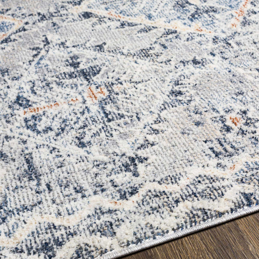 Close-up of the Balamban Area Rug showing its brick red, cream, denim, and gray bohemian pattern and soft polyester texture. Texture
