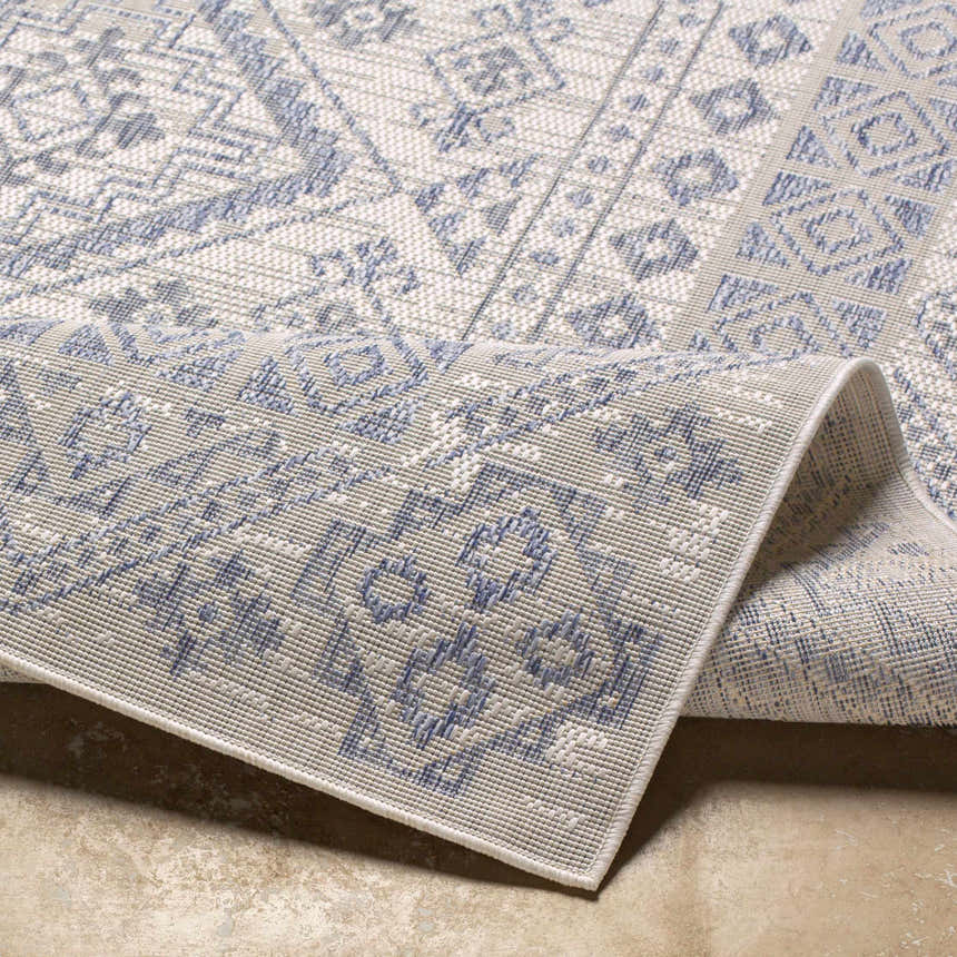 Close-up of the Balarim Indoor & Outdoor Rug showing its gray and blue geometric pattern and durable polypropylene texture. Fold