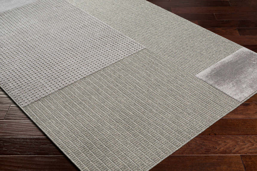 Close-up of the Bantiqui Area Rug showing its geometric pattern and textured weave in neutral tones on a dark wood floor. Corner
