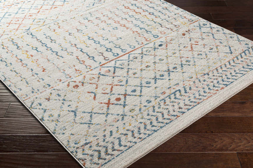 Close-up of Barossa Area Rug: gray, pale pink, rust, and teal geometric pattern on a textured, off-white rug. Corner