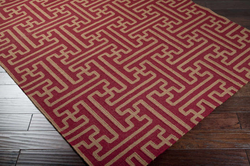 Close-up of the Bentonville Area Carpet. Brick red wool rug with a tan geometric pattern on dark wood floors. Corner