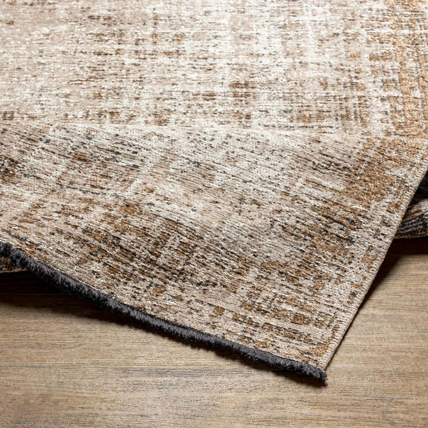 Close-up of Binh Rustic Brown Rug showing charcoal fringes and tan, cream, and brown textured pattern. Fold