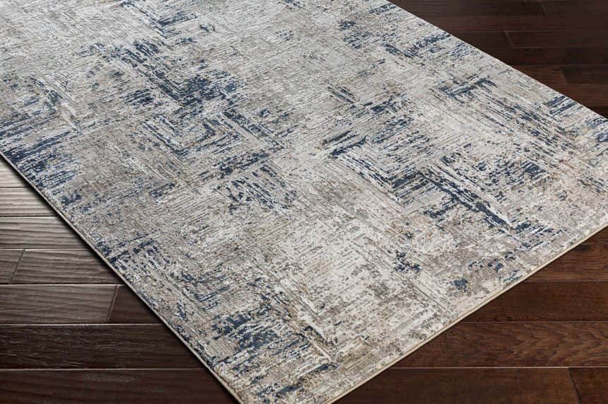 Close-up of the Balasing Area Rug on dark wood floor. Abstract design with dark gray, ivory, and tan colors. Contemporary style. Corner