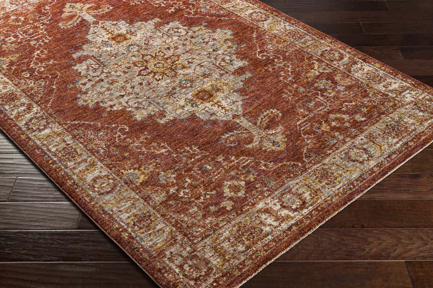 Close-up of the Bluewell Area Rug. Brick red rug with charcoal, beige, and rust traditional pattern on dark wood floor. Corner