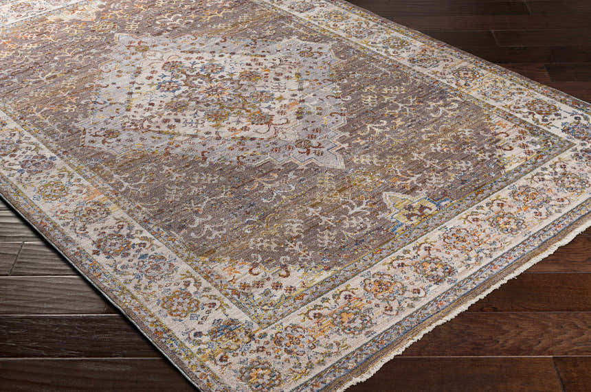 Close-up of the Bourget Area Carpet. Bohemian style rug in brick red, cream, and blue on a dark wood floor. Corner