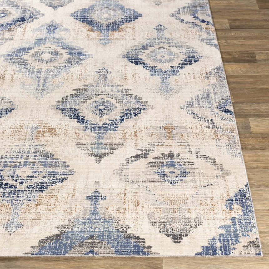 Close-up of the Buckner Blue Ikat Rug, a machine-woven rug with a geometric diamond pattern in blue, brown, and gray on a cream background. Front