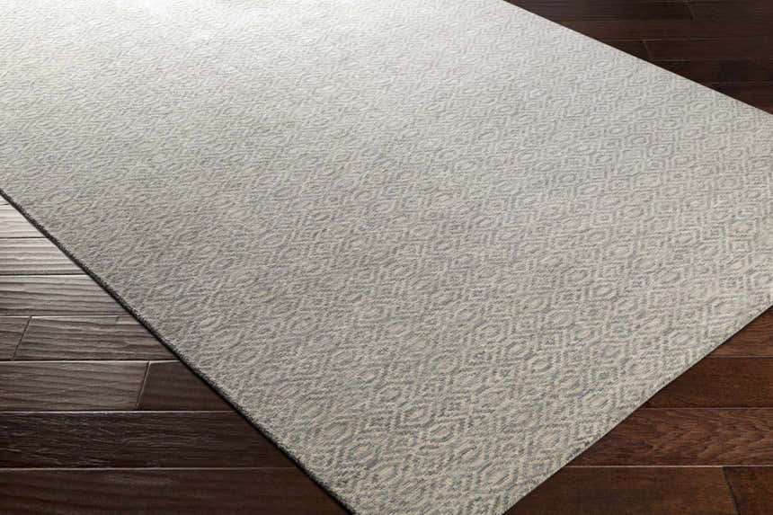 Close-up of the Bumpass Area Rug. Light sage and medium gray wool rug with a subtle geometric pattern on dark wood floors. Corner
