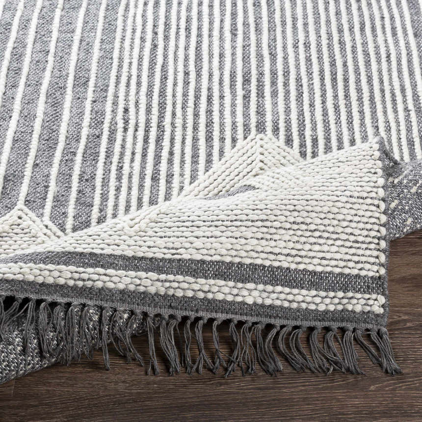 Close-up of the Aldbourne Gray Tassel Flatweave Wool Rug showing charcoal, gray, and ivory stripes and tassel fringe. Fold
