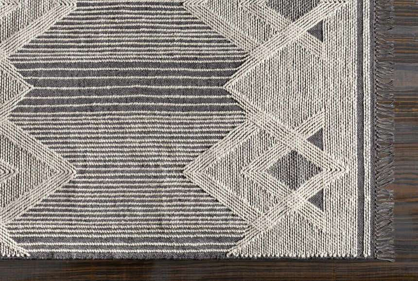 Close up of Aldbourne Gray Tassel Flatweave Wool Rug showing geometric design, stripes, and tassels. Charcoal and ivory tones. Corner