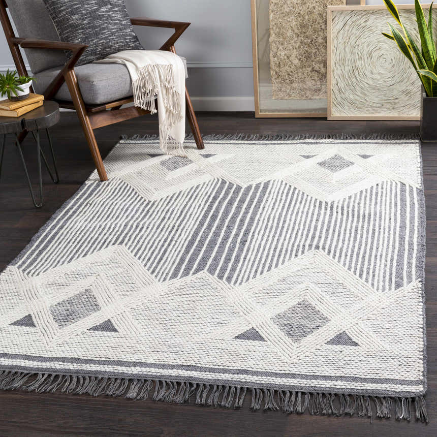 Living room scene with gray chair and Aldbourne Gray Tassel Flatweave Wool Rug, featuring geometric pattern and fringe. Roomscene-Rectangle