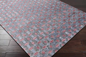 Close-up of the Byfield Carpet showing a geometric pattern in charcoal, dark red, and ink blue on dark wood flooring. Corner