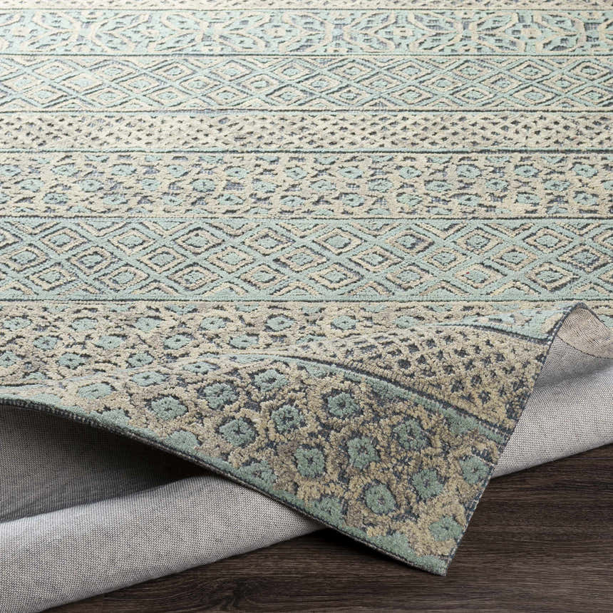 Close-up of the Byron Area Rug showing beige, charcoal, and sage colors with a bohemian-inspired geometric pattern. Fold