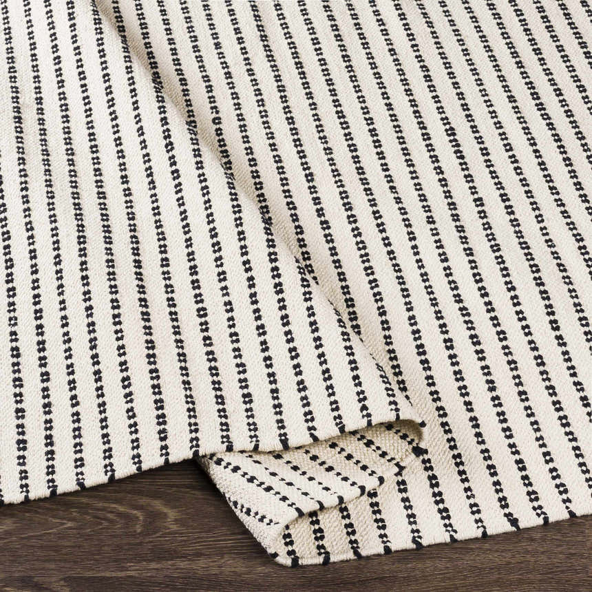 Close-up of the hand woven Calumpang Area Carpet. Beige cotton rug with black striped Southwestern design. Fold